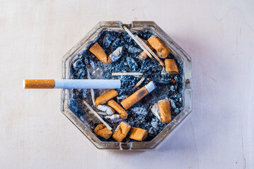 A cigarette with a filter in a dirty ashtray with cigarette butts, conceptual photography,