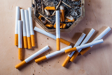 A dirty ashtray with cigarette butts scattered filter cigarettes on a wooden table,