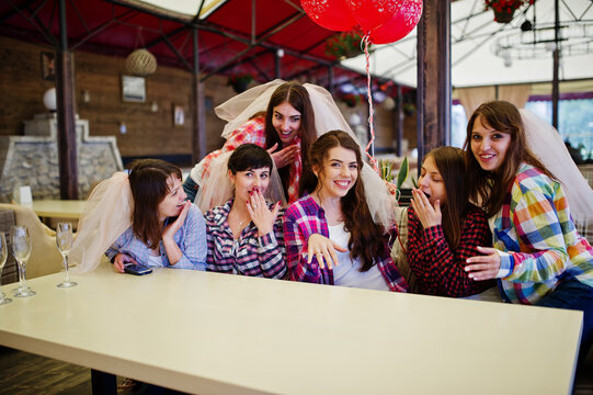 Group of cheerful girls at checkered shirts sitting at table on hen party. Girl showing her engagement ring.