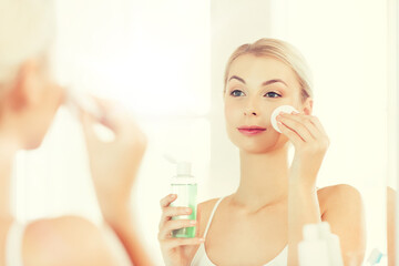 young woman with lotion washing face at bathroom