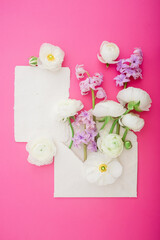 Beautiful flowers and paper cards on pink background. Flat lay, top view. Decorated concept for wedding or beauty blog