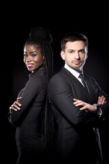 Multi ethnic man and woman standing back to back. Man and woman in black suits on dark background. Dark skinned female together with european man.