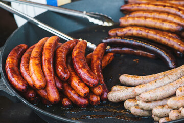 Fried sausages in big frying pan at seasonal fair. Street food.