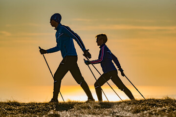 a couple doing Nordic walking exercise on a sunset - obrazy, fototapety, plakaty