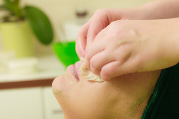 Fototapeta premium Beautician wiping off green mask on woman