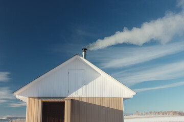 Facade of a small frame house on a background of blue sky. The smoke from the chimney.