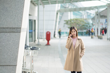 Charming beautiful asian business woman smile in casual style using smartphone for travel with blur the airport terminal.