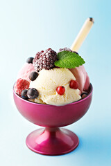 Ice cream with frozen fruit in a purple bowl. Red fruit. Blue background