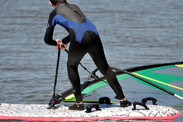 Ein Windsurfer stehend auf dem Surfboard zieht das Segel aus dem Wasser