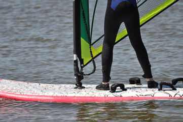Ein Windsurfer stehend auf dem Surfboard hält das Segel, dabei gleitet er auf dem Wasser