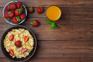The concept of a healthy diet: cornflakes, strawberries and a glass of juice on an old wooden table, free space.