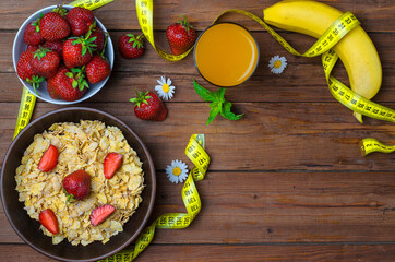 Concept diet food: cereal, strawberries, a banana and a glass of juice on a wooden table.