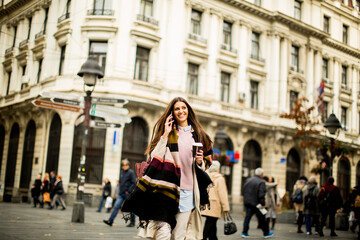 Woman with coffee to go and mobile phone in hand walking down the street