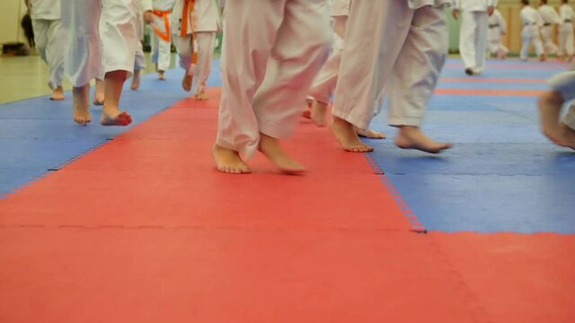 Group of karateka teenagers in kimono runs on tatami in the gym