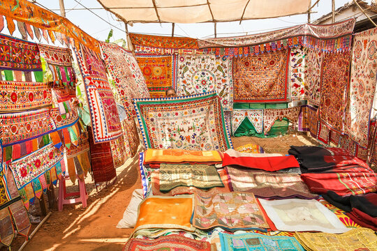 Seller of antique carpets shows colorful embroidered bedspreads at the marketplace of oriental bazaar