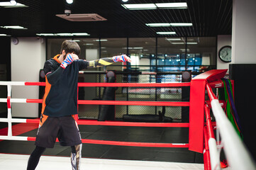 Obraz premium Professional Muay Thai fighter. Male boxer in training sportswear, an exercise in sports hall, fight with a shadow in ring, Strike testing