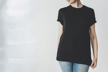 Mock-up of black cotton t-shirt, white wall in the background, Young hipster girl wearing black long t-shirt with blank space for your logo or design