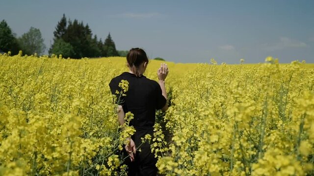 Young Woman in Black clothes overalls Running through Yellow Field Touching Flowers HD