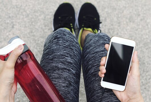 Female Runner Holding Smart Phone And Water Bottle While Taking Break. (Color Processed)