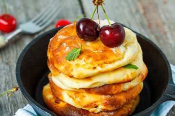 Homemade cottage cheese pancakes with cherries in a cast-iron frying pan. Russian dessert from cottage cheese.