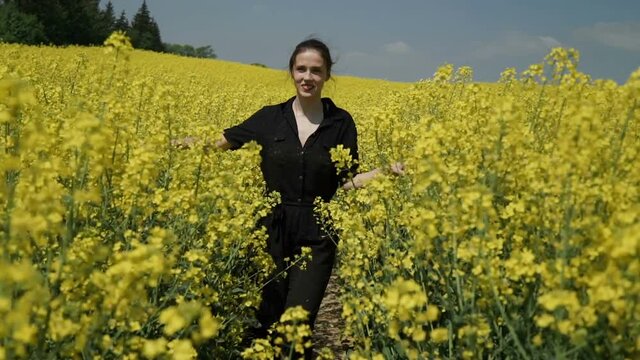 Young Woman in Black clothes overalls Running through Yellow Field Touching Flowers HD