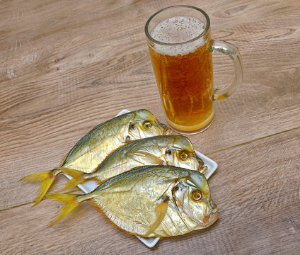 Dried fish and a glass of beer on a wooden table.