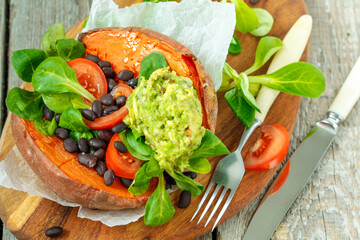 Baked whole sweet potato with guacamole and black beans in a cast-iron frying pan. Love for a healthy vegan food concept