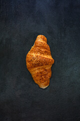 Top view of fresh brown croissant isolated on gray stone slate background