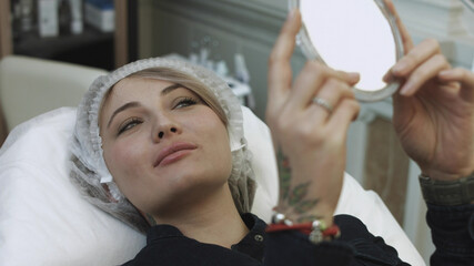 Patient looking at herself in the mirror after the lip augmentation procedure