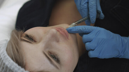 Beautician removes blood from the patient's mouth during the procedure of the lips augmentation