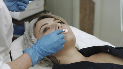 Professional beautician puts on the lips of the patient cream