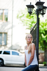 Stylish blonde woman wear at jeans, glasses, choker and white shirt against luxury car. Fashion urban model portrait.