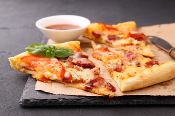 Pizza with sausage, ham, tomato and cheese, decorated with basil and cut into pieces on a parchment