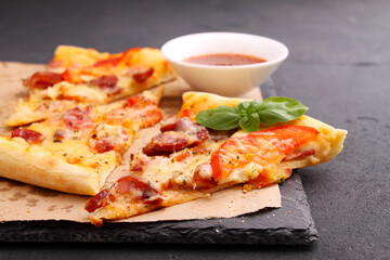 Pizza with sausage, ham, tomato and cheese, decorated with basil and cut into pieces on a parchment