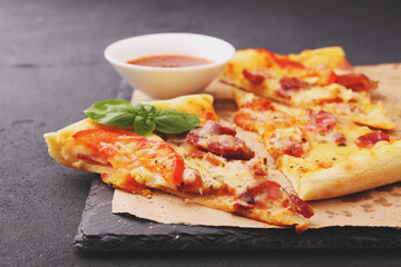 Pizza with sausage, ham, tomato and cheese, decorated with basil and cut into pieces on a parchment
