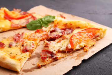 Pizza with sausage, ham, tomato and cheese, decorated with basil and cut into pieces on a parchment