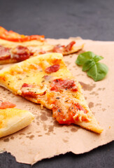 Pizza with sausage, ham, tomato and cheese, decorated with basil and cut into pieces on a parchment