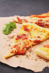 Pizza with sausage, ham, tomato and cheese, decorated with basil and cut into pieces on a parchment