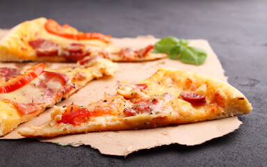 Pizza with sausage, ham, tomato and cheese, decorated with basil and cut into pieces on a parchment