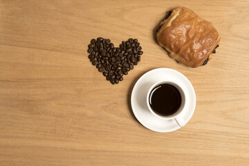 Black coffee in a cup and saucer with a croissant and coffee beans