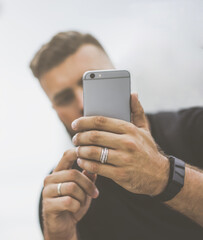 Close-up of smartphone in hands of young bearded man hipster. In background, guy's face is in soft focus.