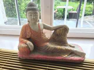 eine Buddha-Statue, die seitlich sitzt und die linke Hand auf dem linken Knie ruht, das nach hinten...