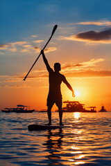Paddle boarder. Black sunset silhouette of young sportsman paddling on stand up paddleboard. Healthy lifestyle. Water sport, SUP surfing tour in adventure camp on active family summer beach vacation.