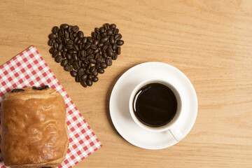 Black coffee in a cup and saucer with a croissant  and coffee beans 
