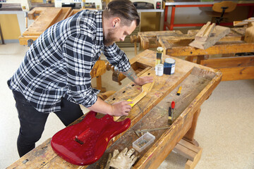 Craftsman sanding a guitar neck in wood at workshop