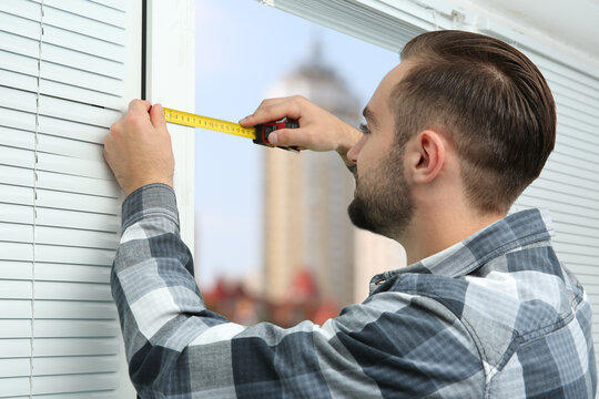 Young man taking measure of window for blinds installation at home