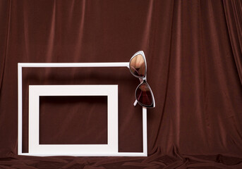 Two empty picture frames and glasses on background of brown cloth.