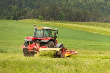 Work on an agricultural farm. A red tractor cuts a meadow.
