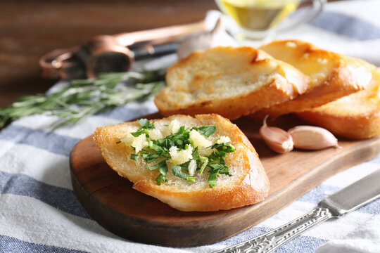Tasty bread slices with garlic and herbs on wooden cutting board