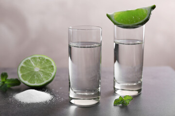 Tequila shots with juicy lime and salt on grey background